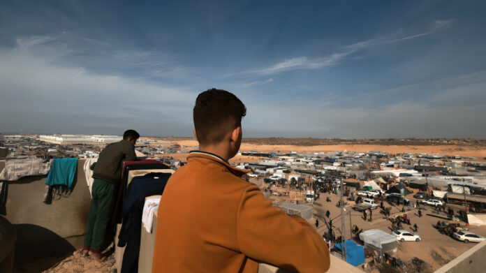 فلسطينيان أعلى سطح منزل ينظران إلى خيام أقامها نازحون فروا من خان يونس في رفح، بالقرب من حدود غزة مع مصر.‏