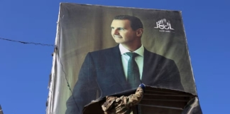 بعيدًا عن الشعب السوري.. المستفيدون من انهيار نظام الأسد مسلح يُزيل صورة بشار الأسد (وكالات)