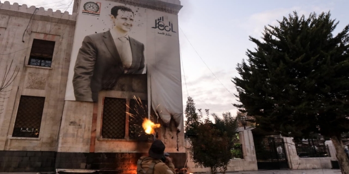 معارض سوري يرمي صورة بشار الأسد على مبنى بلدية حماة بالرصاص في أعقاب سيطرة قوات فصائل المعارضة على المدينة، في 6 ديسمبر 2024. (وكالات)